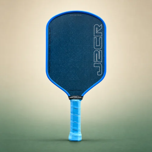 Honolulu J2CR Crystal Blue Endurance 16mm Pickleball Paddle, front view on a sand and green studio background Honolulu J2CR Crystal Blue Endurance 16mm Pickleball Paddle, front view