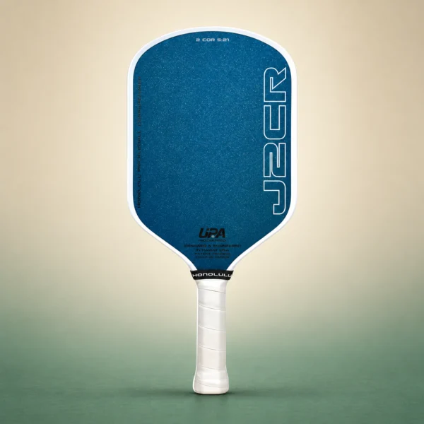 Honolulu J2CR Crystal Blue Endurance 16mm Pickleball Paddle - White, front view on a sand and green studio background Honolulu J2CR Crystal Blue Endurance 16mm Pickleball Paddle - White, front view