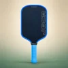 Honolulu J6CR Crystal Blue Endurance 16mm Pickleball Paddle, front view on a sand and green studio background Honolulu J6CR Crystal Blue Endurance 16mm Pickleball Paddle, front view
