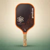 Proton Project Coyote Elongated 15mm Pickleball Paddle, front view on a sand and green studio background Proton Project Coyote Elongated 15mm Pickleball Paddle, front view